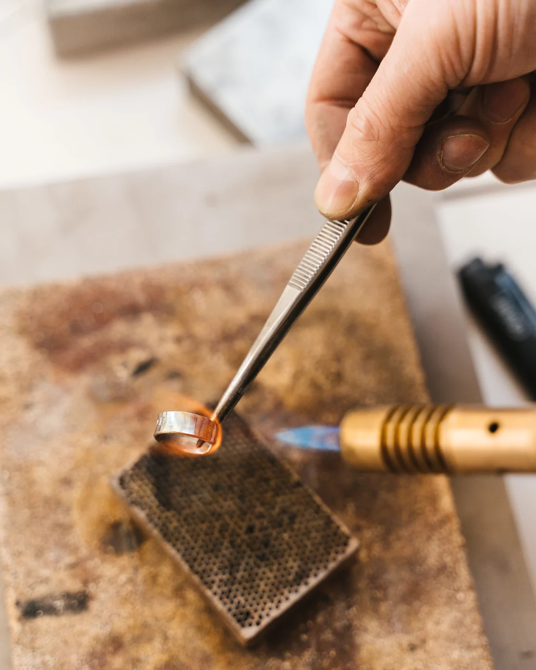 A jeweller working a gold band at the bench under a torch