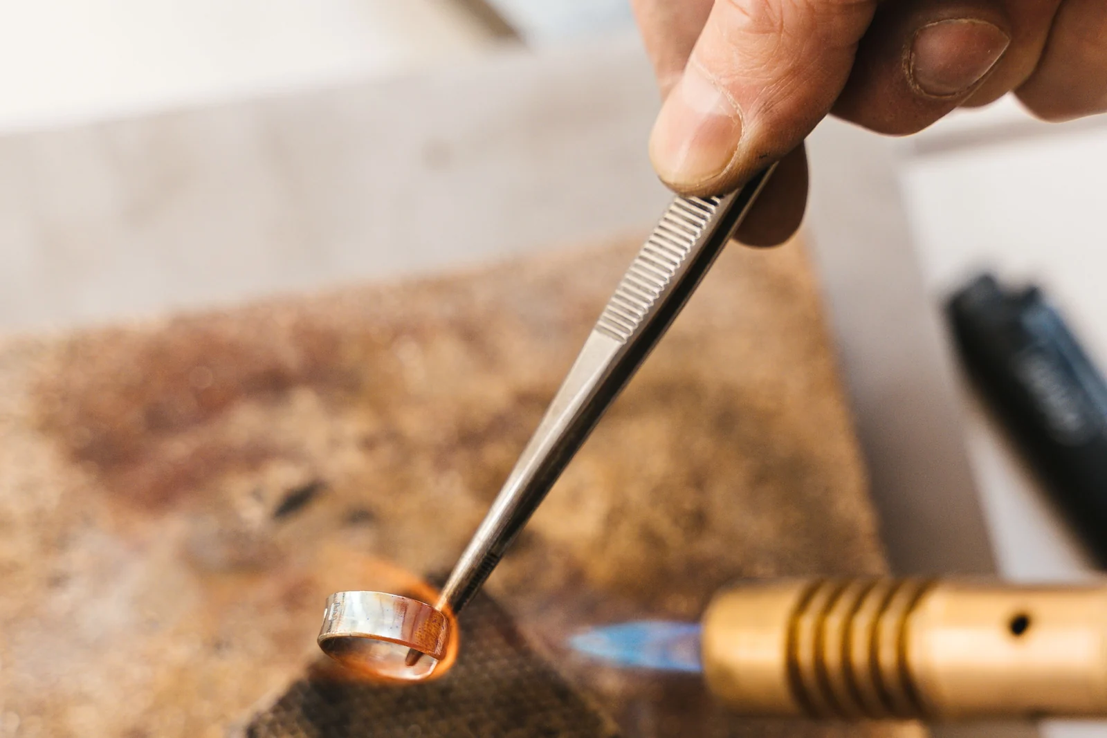 A jeweller working a gold band at the bench under a torch