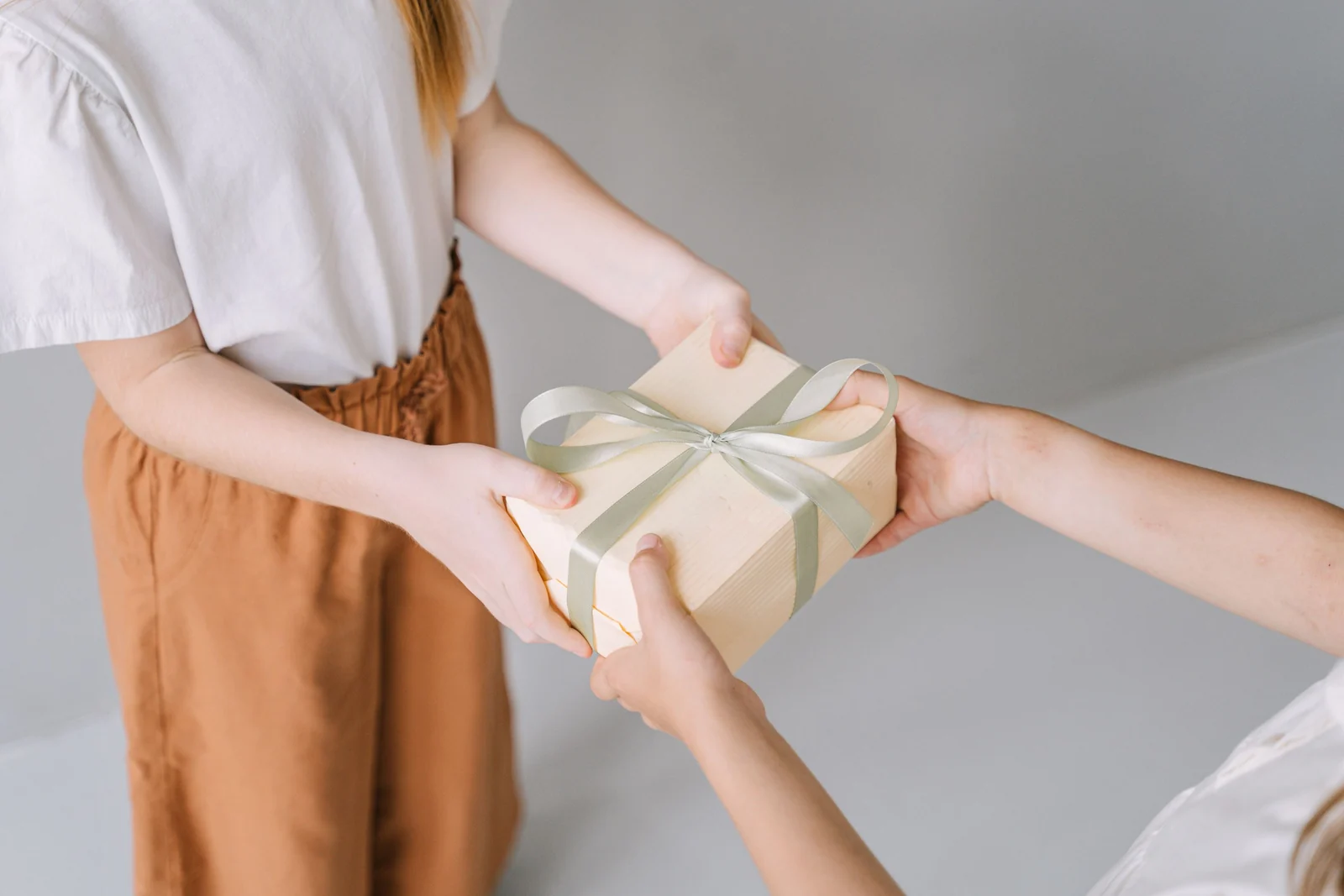A wrapped gift box passed from one pair of hands to another